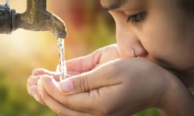 Young person drinking from an outdoor water faucet
