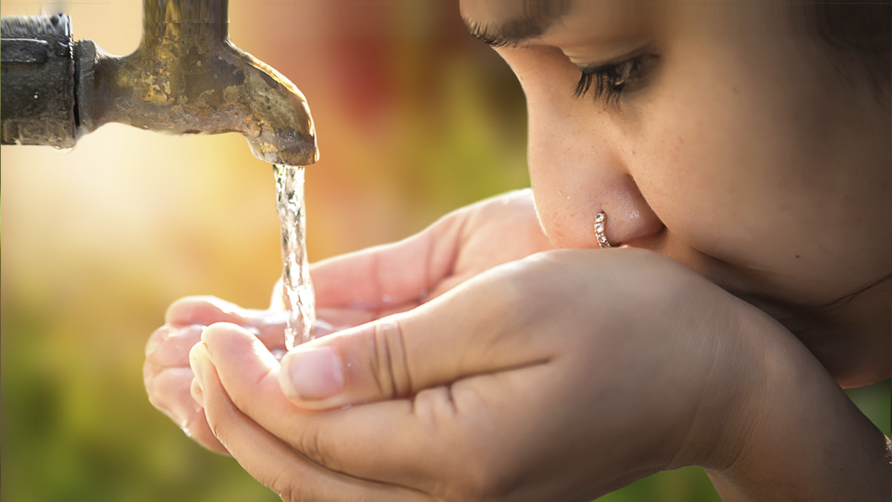 Young person drinking from an outdoor water faucet