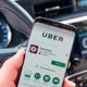 Uber driver inside car with ridesharing app displayed on smartphone.