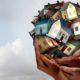 Composite of hands lifting up several toy houses. Image meant to convey affordable housing