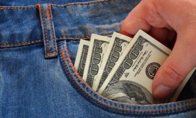 Photo depicting wage theft: a hand reaching to take $100 bills out of a pockett