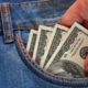 Photo depicting wage theft: a hand reaching to take $100 bills out of a pockett