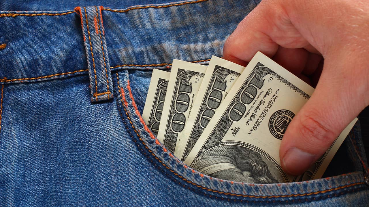 Photo depicting wage theft: a hand reaching to take $100 bills out of a pockett