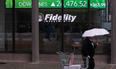 Photo of a man walking in the rain past the stock ticker scroll board