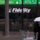 Photo of a man walking in the rain past the stock ticker scroll board