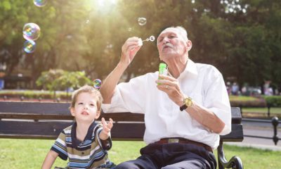 Photo of child with older man blowing bubbles in a park