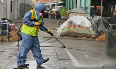 Photo of a city worker cleaning the sidewalk by a tent city