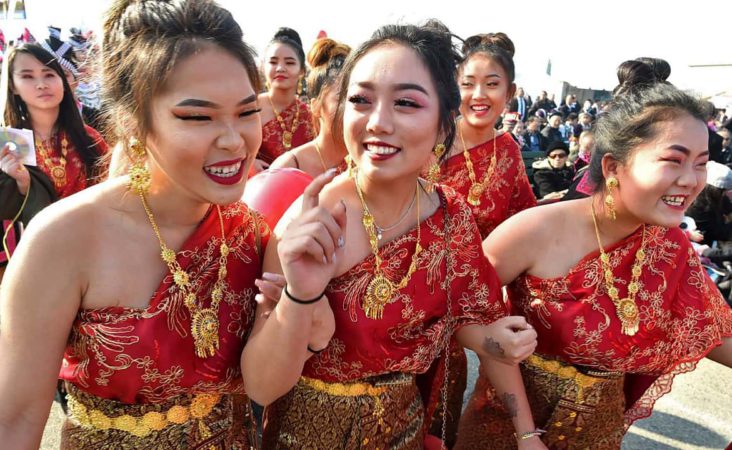 In this photo taken Dec. 26, 2017, from left front, Kathy Vang, Suleka Cha, and Der Vue, McLane High students have fun as they walk in the grand opening parade during the Hmong Cultural New Year Celebration at the fairgrounds in Fresno, Calif. The country's small Hmong American population is reeling from the shooting deaths of four men at a backyard party at a Northern California central valley city. Fresno hosts a week-long New Year's party every year that draws tens of thousands of Hmong from around the country, complete with colorful traditional dress, song, and sports games. (John Walker/The Fresno Bee via AP)