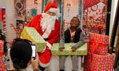 Photo of a young student sitting next to Santa Claus with a wrapped gift