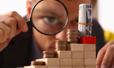 Photo of a man looking through a magnifying glass at small amounts of moneylas